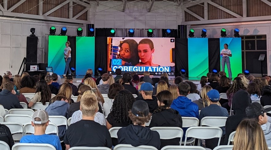 Stage with people speaking and crowd of younger people watching