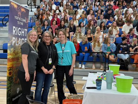 three smiling women standing next to a huge banner in front of a large group