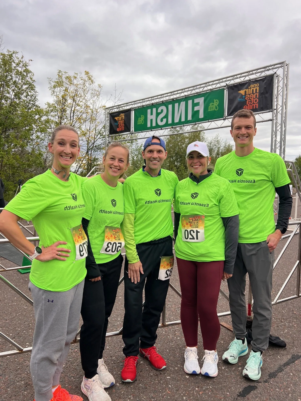 a group of five in green t-shirt, standing together and smiling