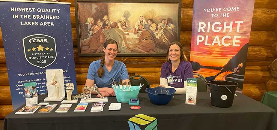 Two smiling women sit at a desk in front of a Right Place banner, with books and materials on the desk.