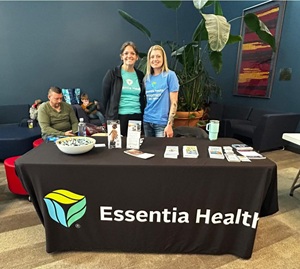 Two Essentia employees smile behind a desk while a man sits nearby.